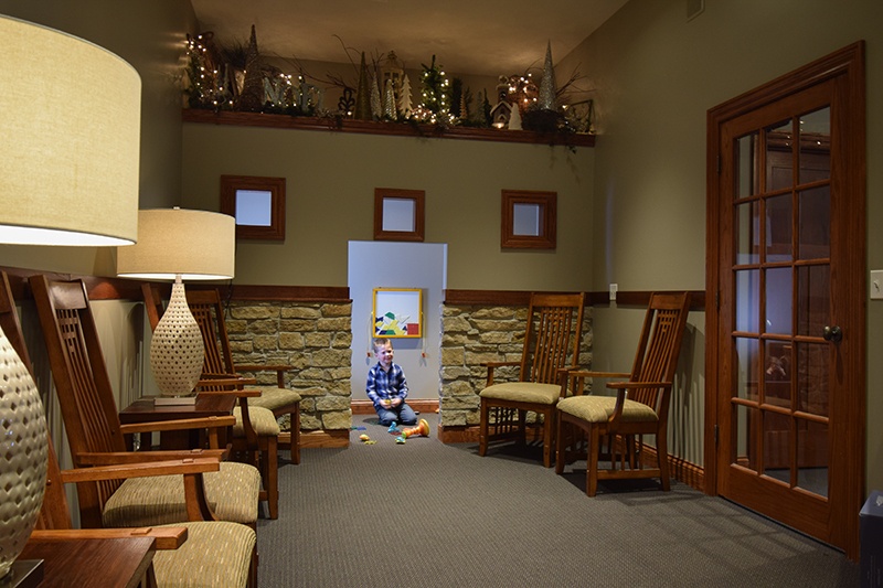 front office seating area with cushioned chairs, decorations, and play area for children, with one boy playing
